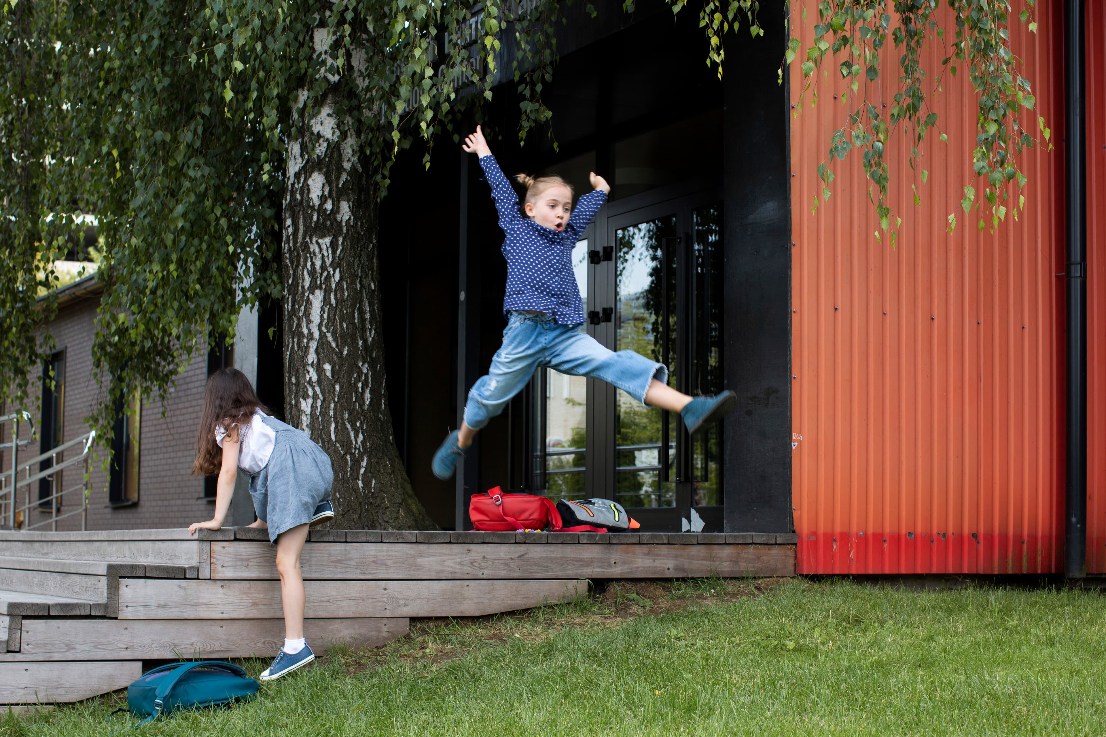 Children playing outside with a young girl leaping in the air.