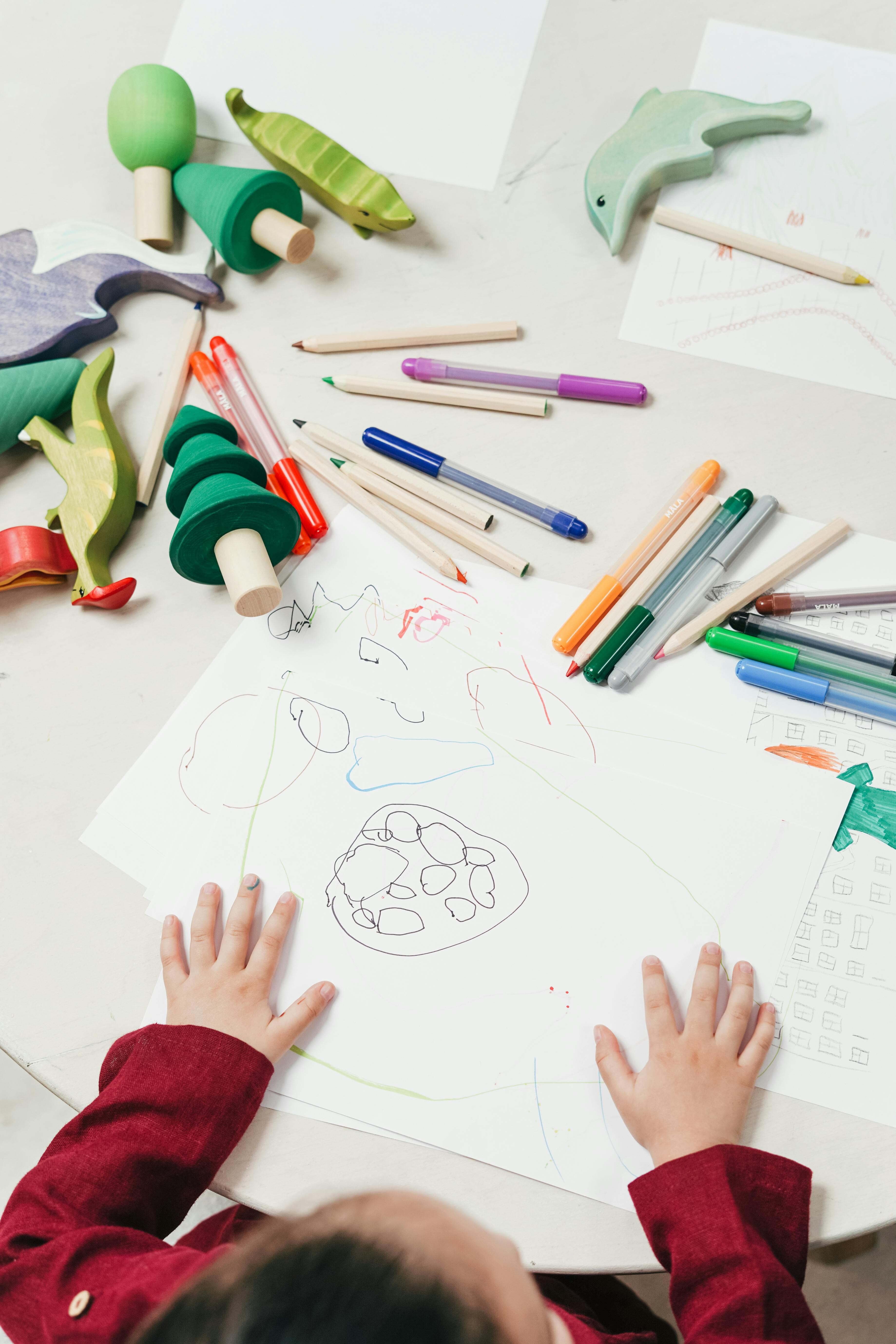 A desk covered in art supplies with a young child's hands visible.