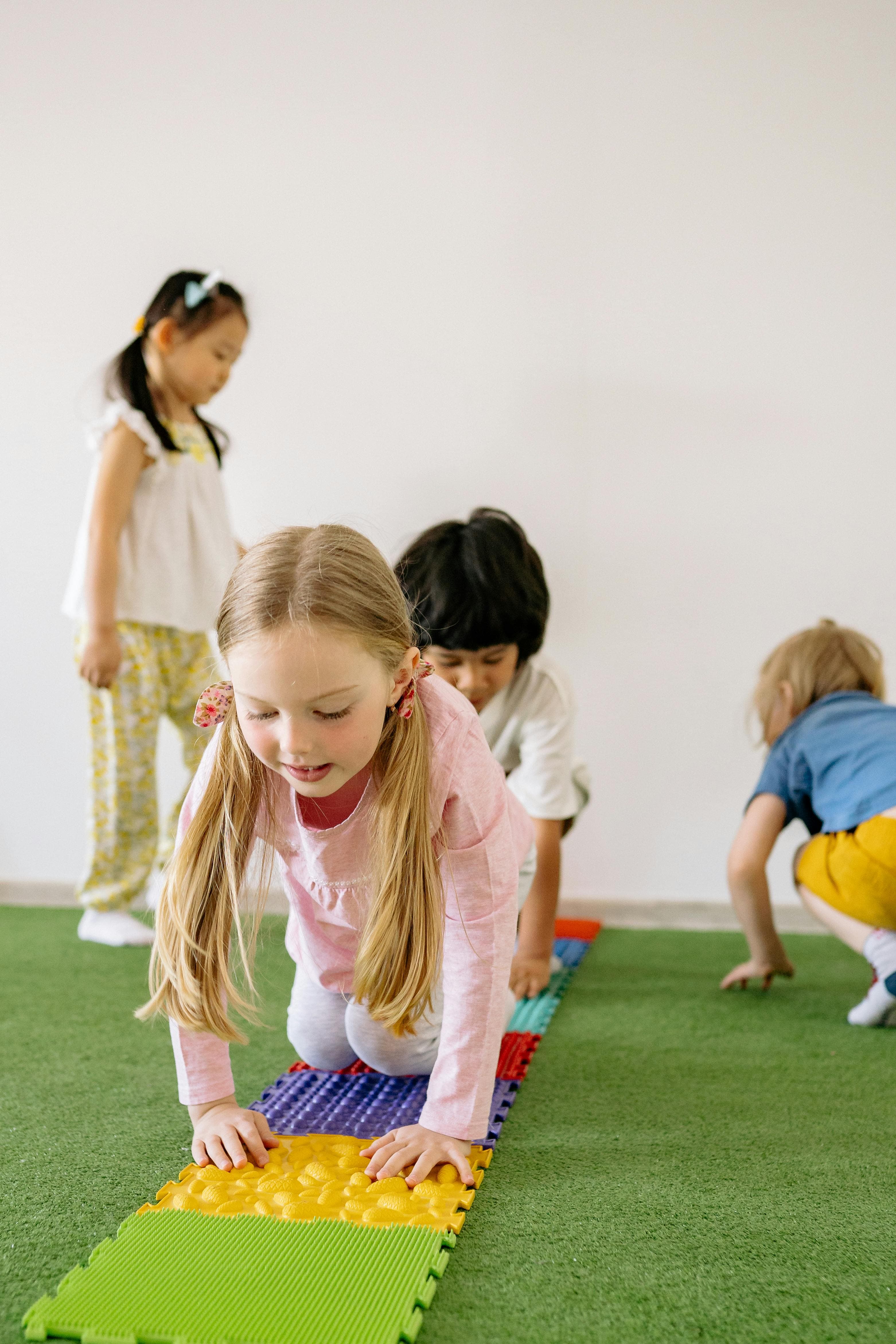 A group of children playing a tile game on a green mat.